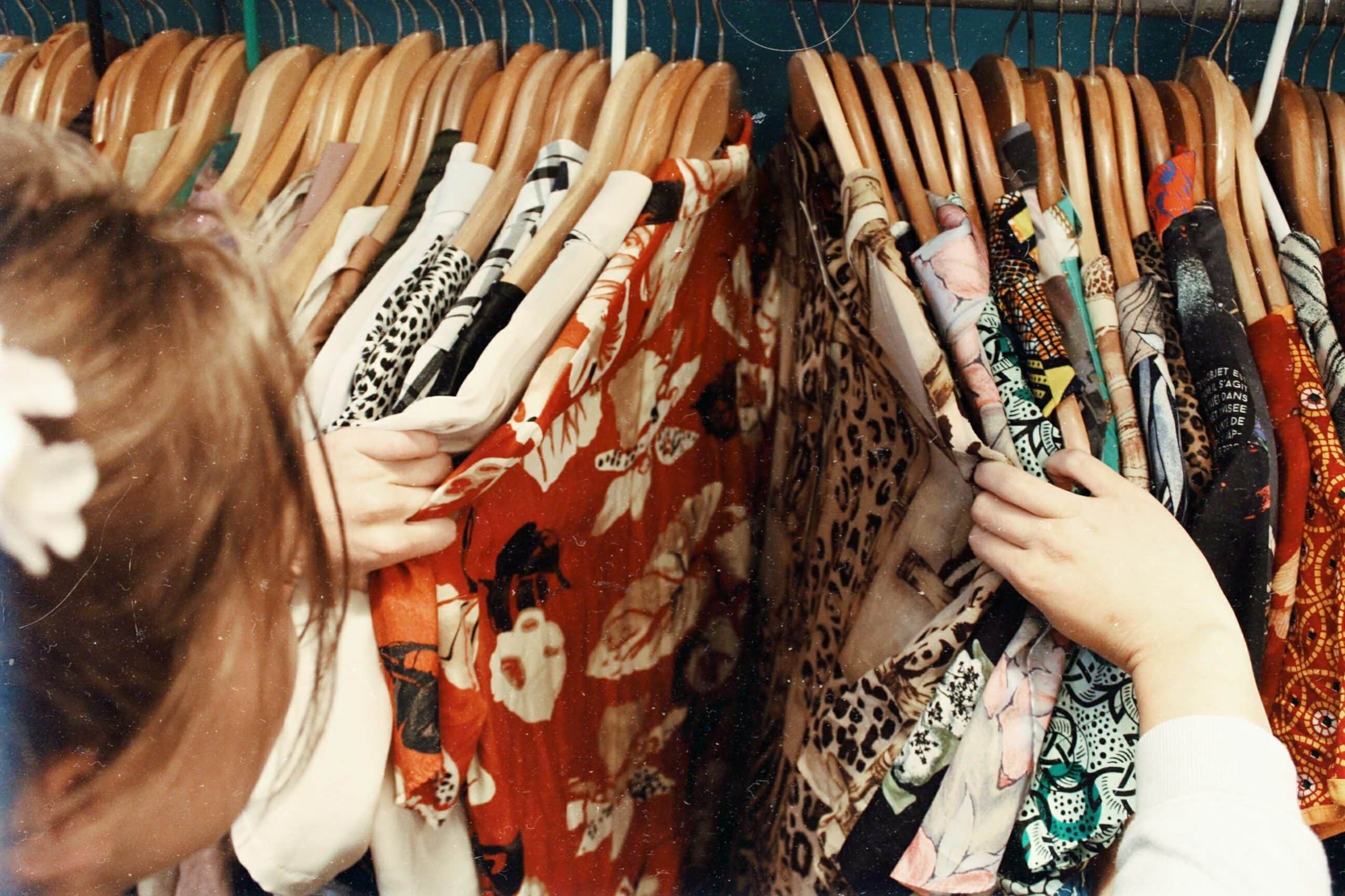 a woman is browsing through assorted styles of shirts and clothing on a rack in a shop